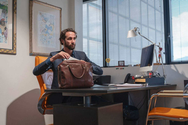 uomo seduto alla scrivania del suo ufficio mentre prende un documento dalla sua borsa in pelle Castelli
